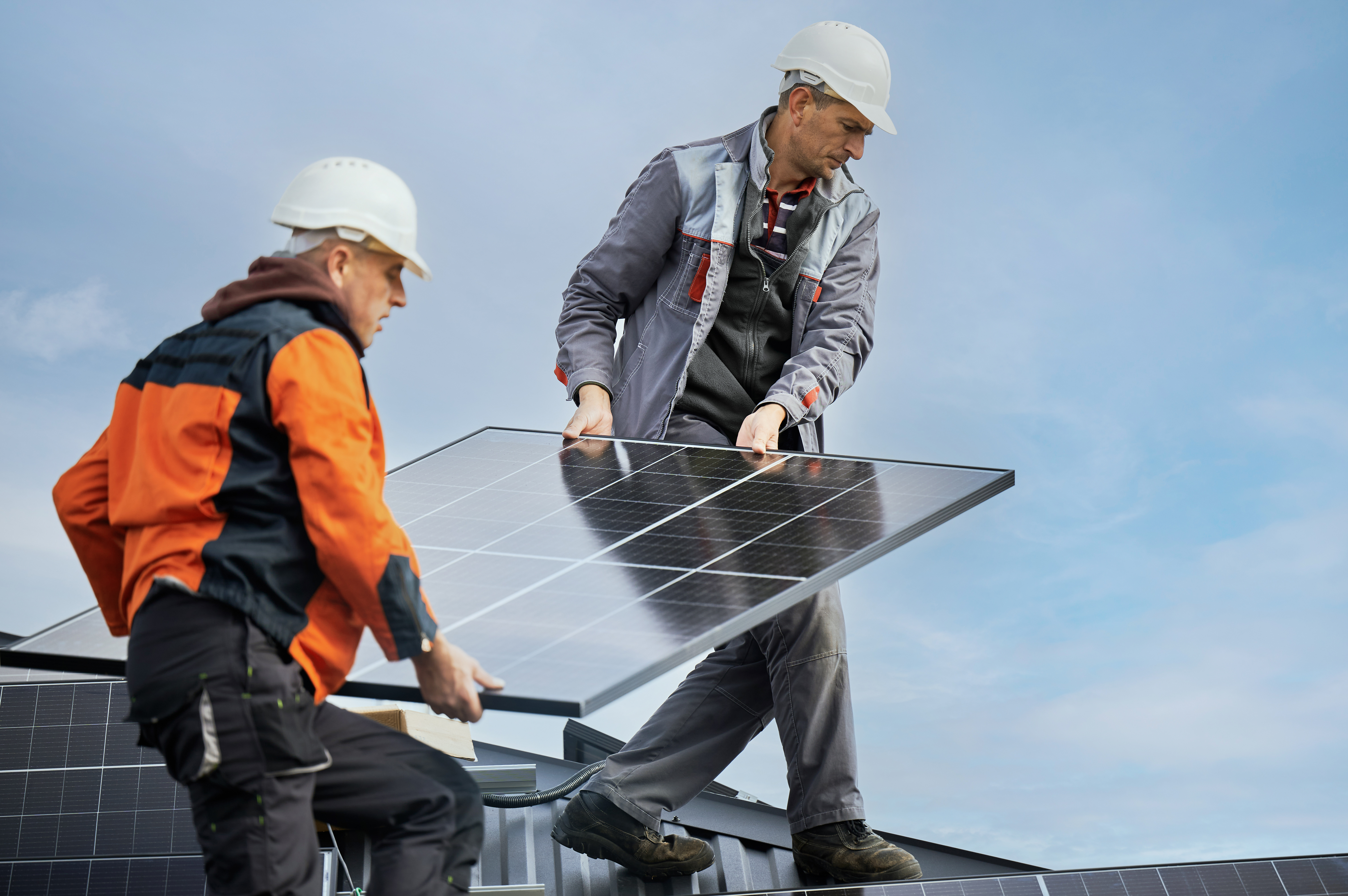 Zwei Handwerker sind auf einem Gebäudedach und tragen ein Solarpanel an Ort und Stelle