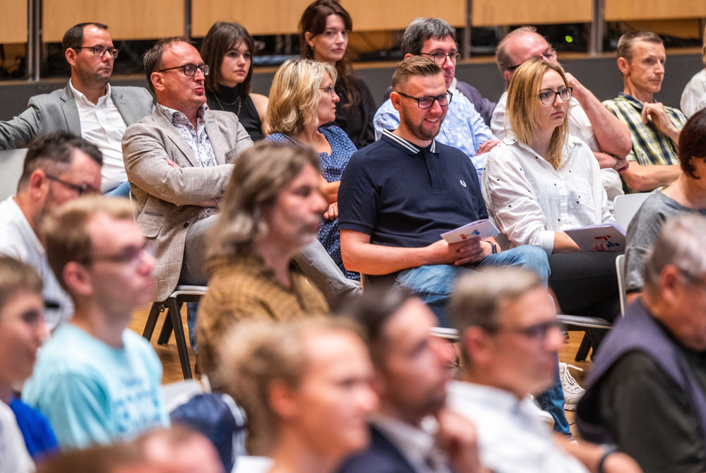 Man sieht ein Bildausschnitt von mehreren Zuhörern einer Konferenz.