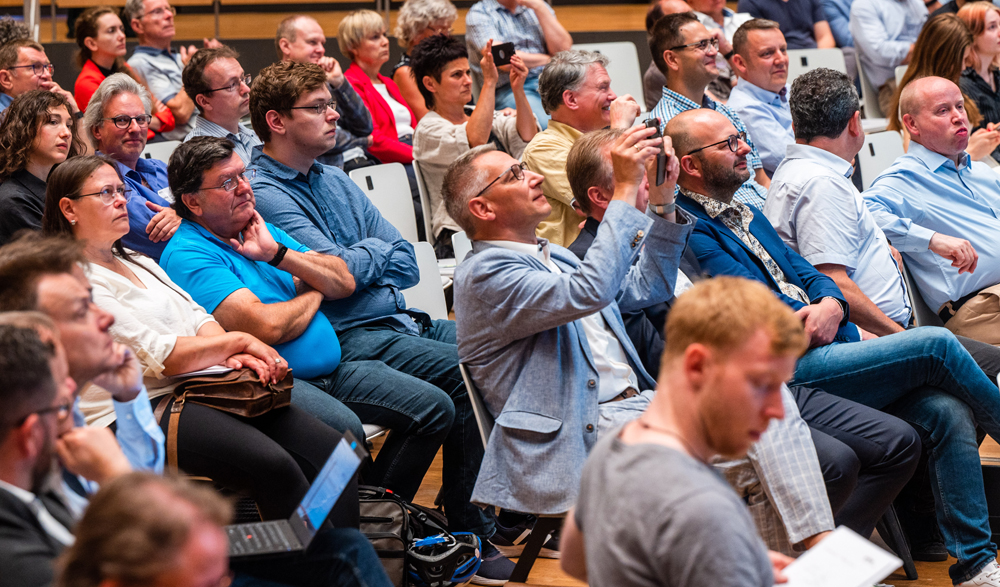 Ein Bildausschnitt einer Gruppe Mitarbeiter, die einen Vortrag anhören. Ein Mitarbeiter macht ein Foto.